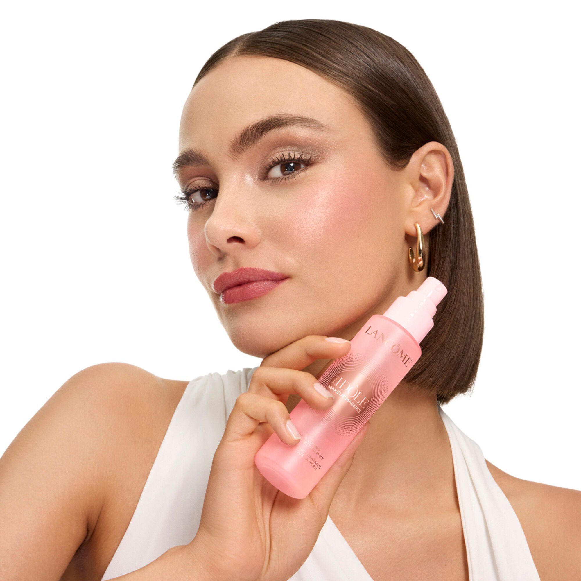 Model holding pink Idole setting mist next to her face.