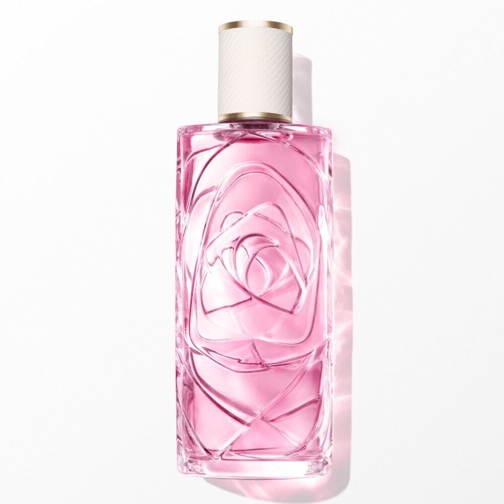 A transparent glass perfume bottle with light pink liquid, textured design, and white and gold cap. Centered vertically on a white background with soft, bright front lighting and a subtle shadow.